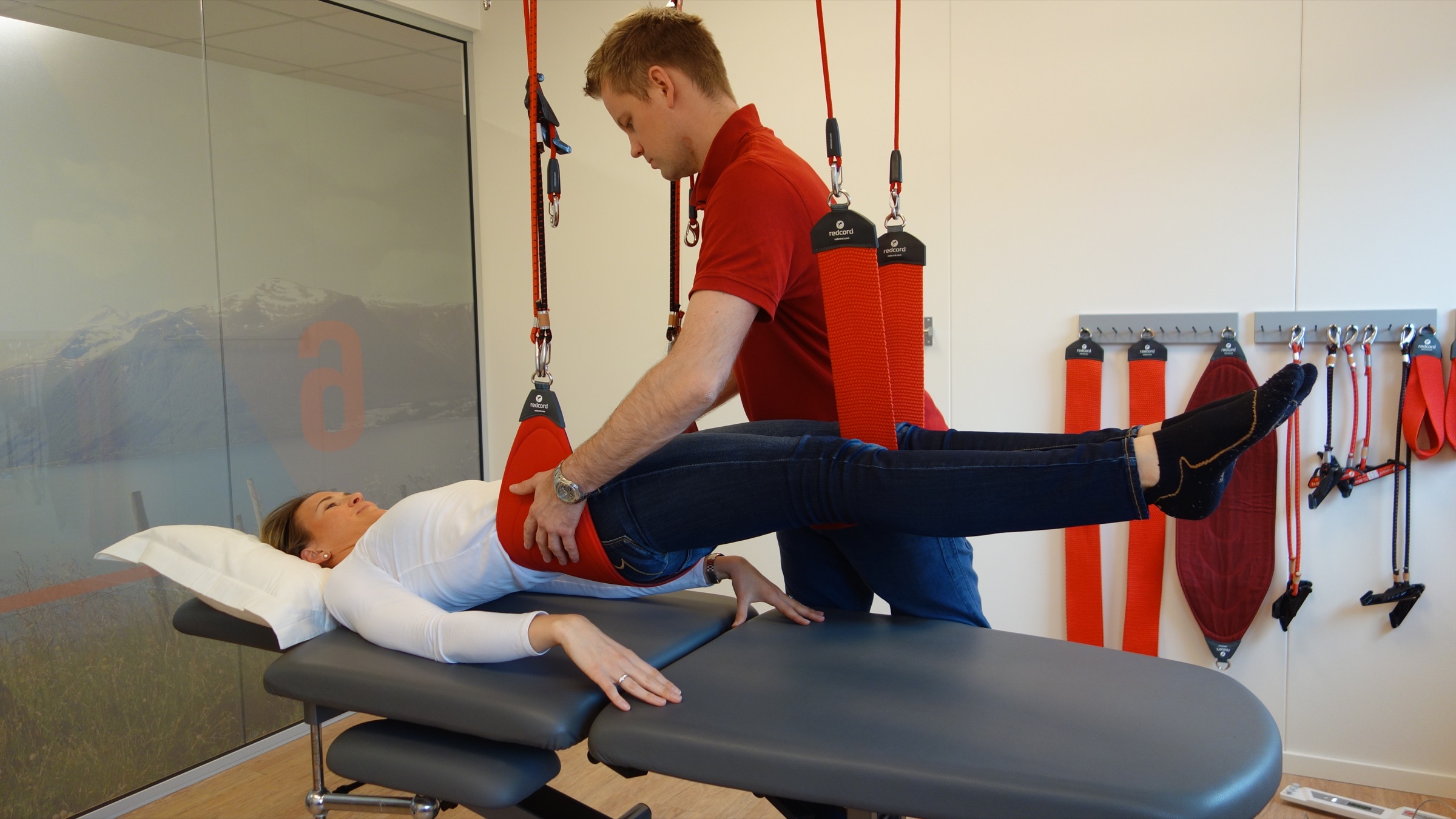 A practitioner supporting a patient's movement on the Redcord Workstation in a clinic